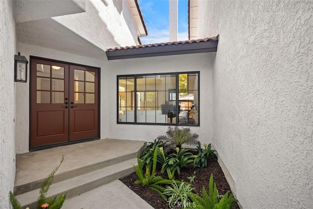 entrance to property with a tiled roof, french doors, and stucco siding