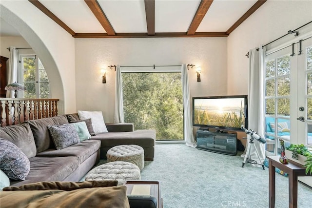 carpeted living room featuring a healthy amount of sunlight, arched walkways, beamed ceiling, and french doors