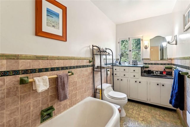 bathroom featuring toilet, a wainscoted wall, vanity, tile walls, and a bathtub