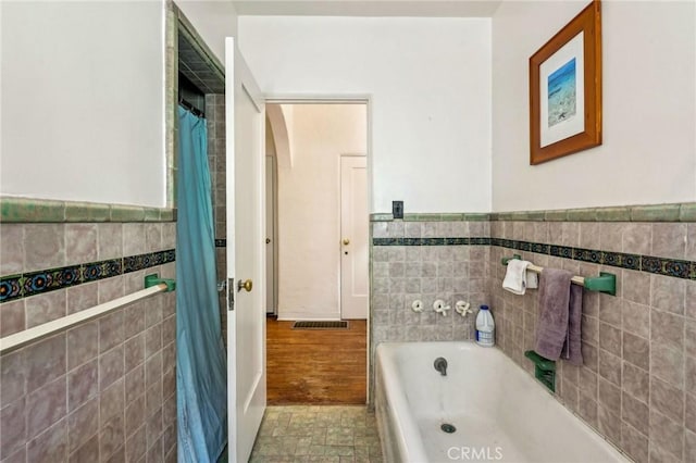 bathroom with a tub to relax in, wainscoting, and tile walls