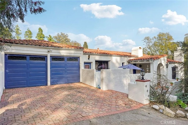 mediterranean / spanish house with a fenced front yard, decorative driveway, a chimney, stucco siding, and a tiled roof