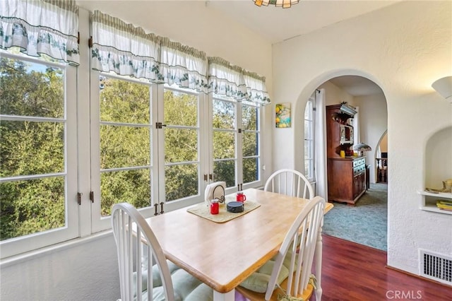 dining room with a wealth of natural light, arched walkways, visible vents, and dark wood finished floors