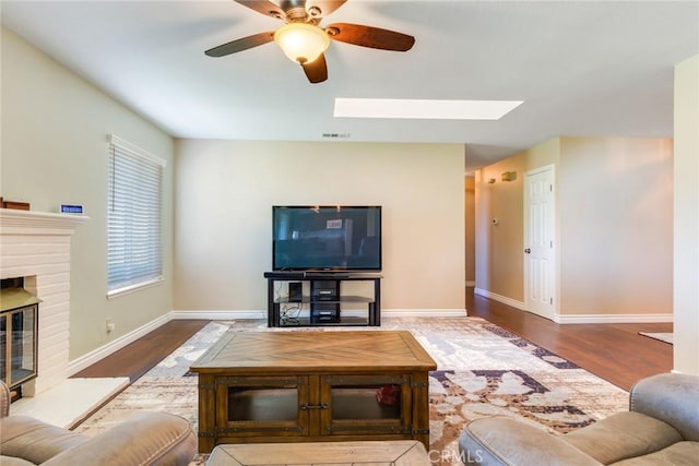 living area featuring ceiling fan, a fireplace, baseboards, and wood finished floors