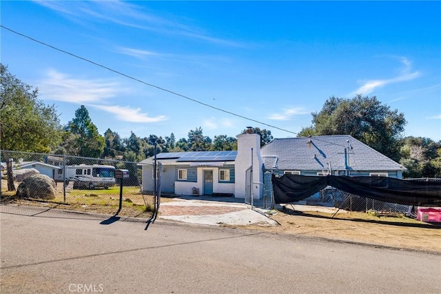 ranch-style house with a fenced front yard, a chimney, and solar panels