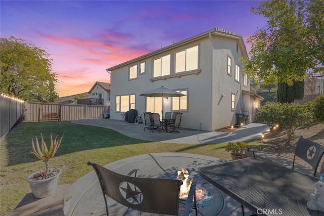 back of house at dusk with a fenced backyard, a yard, a patio, and stucco siding