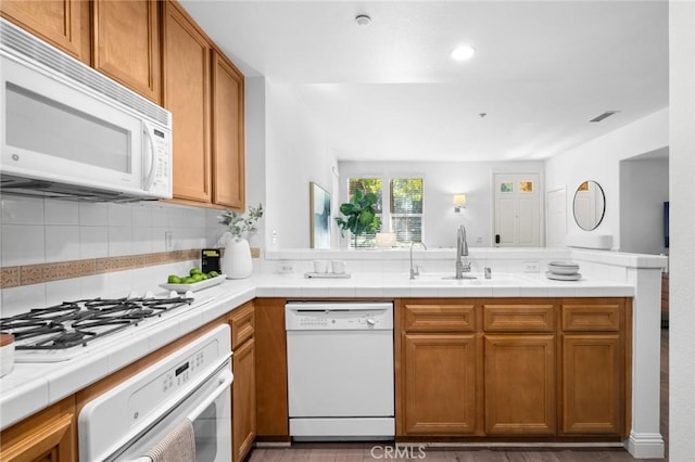 kitchen featuring white appliances, brown cabinets, a sink, and a peninsula