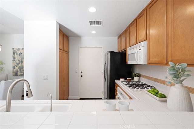 kitchen with white appliances, a sink, visible vents, tile counters, and brown cabinets