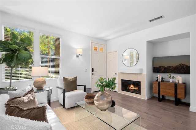 living area featuring a tiled fireplace, wood finished floors, visible vents, and baseboards