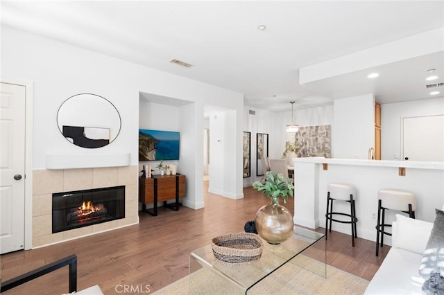 living room with a tile fireplace, visible vents, baseboards, and wood finished floors