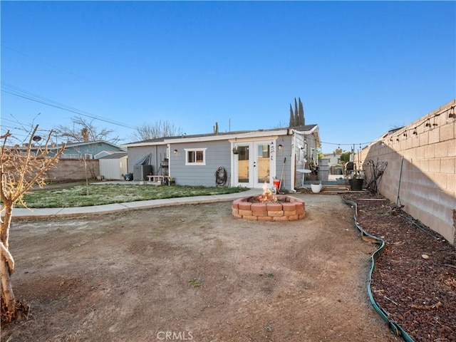 back of property with a fenced backyard, a fire pit, and french doors