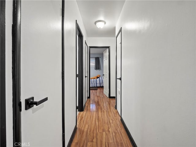 corridor featuring light wood-type flooring and baseboards