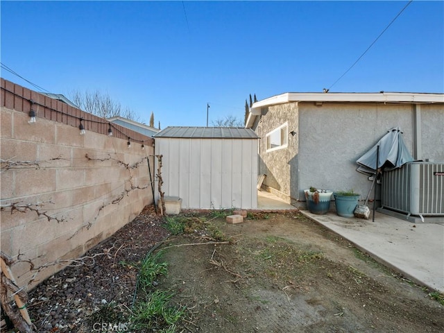 view of yard featuring central AC unit, a fenced backyard, an outbuilding, a patio area, and a shed