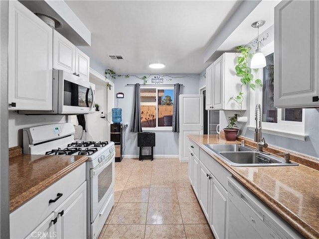 kitchen featuring light tile patterned floors, hanging light fixtures, white cabinets, a sink, and white appliances