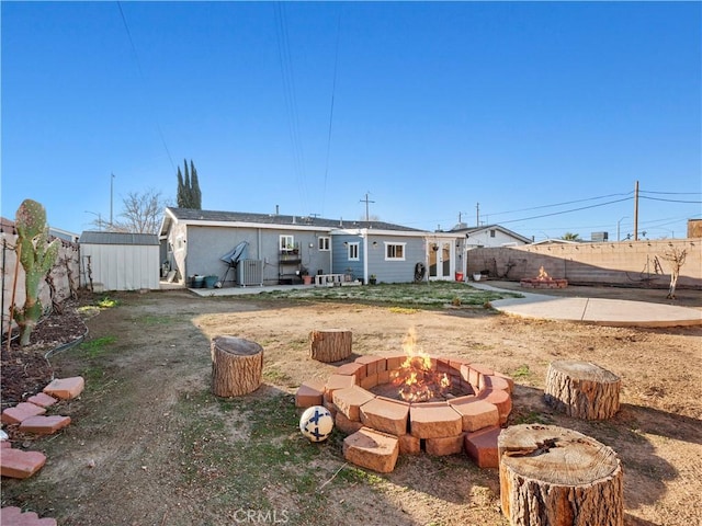 back of house with an outbuilding, a storage shed, central AC, a fenced backyard, and a fire pit