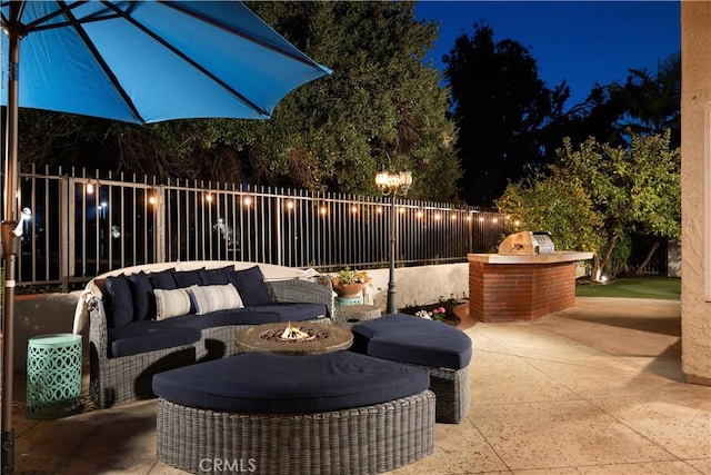 patio at night with an outdoor living space with a fire pit and fence