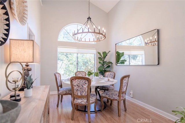 dining room featuring light wood-style floors, baseboards, high vaulted ceiling, and a notable chandelier