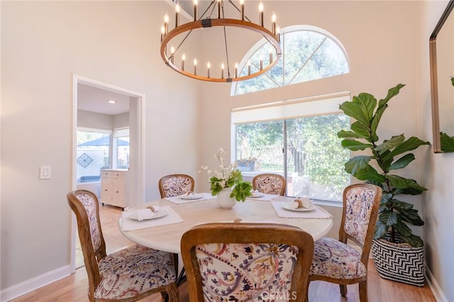 dining area featuring light wood-style floors, baseboards, a high ceiling, and a chandelier