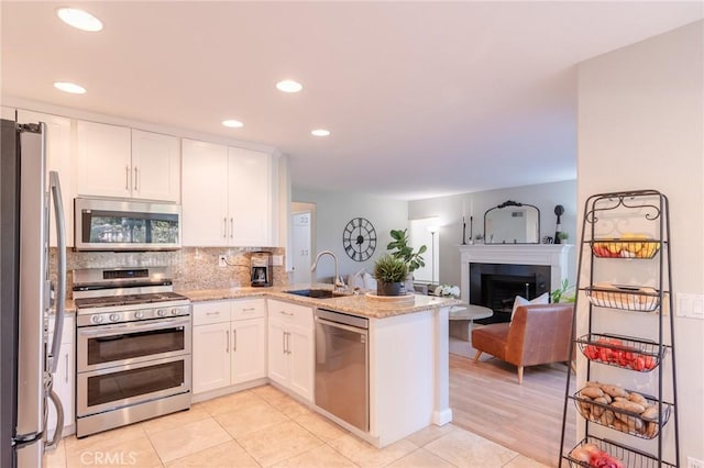 kitchen featuring a peninsula, a sink, white cabinetry, appliances with stainless steel finishes, and tasteful backsplash