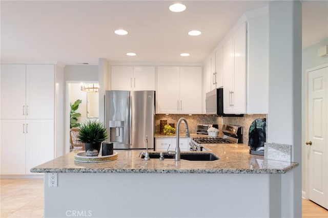 kitchen with tasteful backsplash, appliances with stainless steel finishes, a peninsula, light stone countertops, and a sink