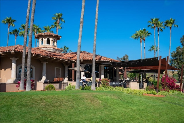 rear view of house with a lawn, a tiled roof, and stucco siding