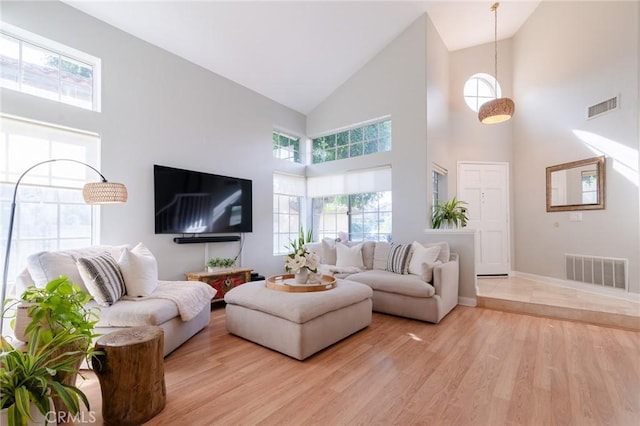 living room featuring high vaulted ceiling, baseboards, visible vents, and light wood finished floors