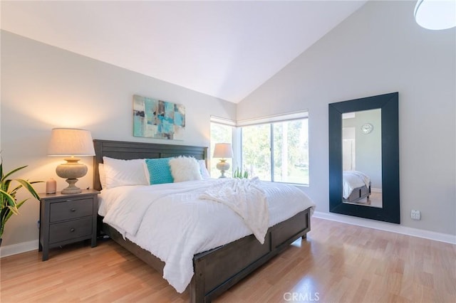 bedroom with high vaulted ceiling, baseboards, and wood finished floors