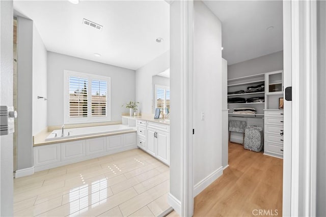 full bath with a garden tub, wood finished floors, vanity, visible vents, and a walk in closet