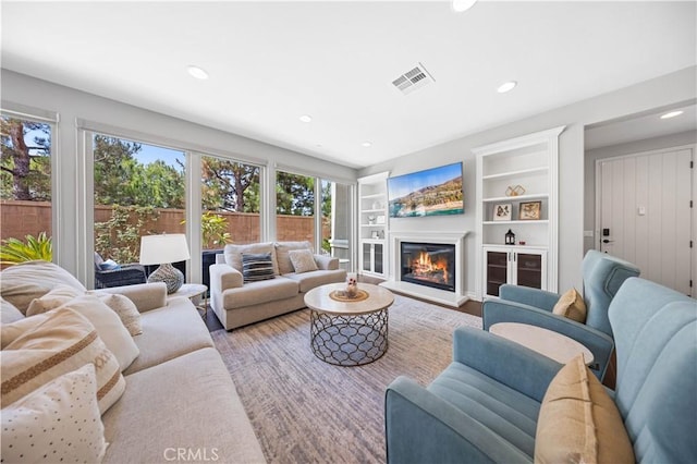 living room featuring built in shelves, recessed lighting, visible vents, a glass covered fireplace, and wood finished floors