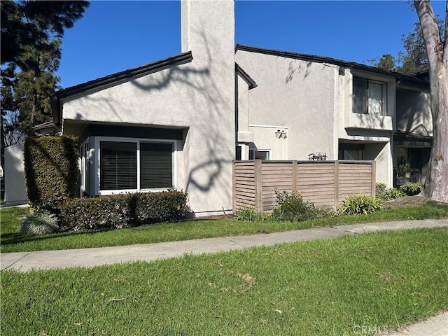 view of home's exterior featuring a yard, fence, a chimney, and stucco siding