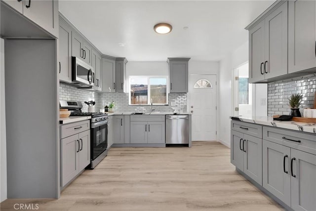 kitchen with light wood-style flooring, stainless steel appliances, backsplash, and gray cabinetry