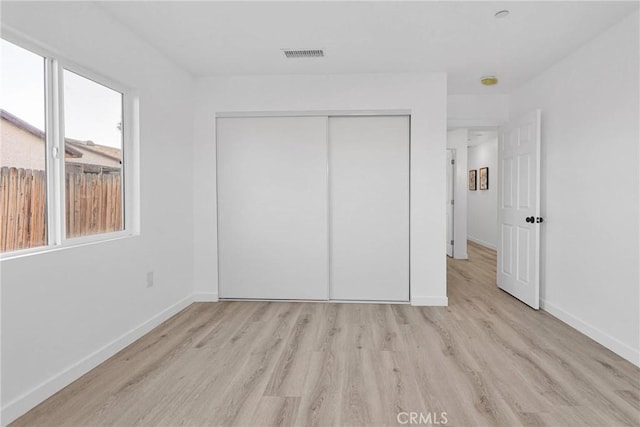 unfurnished bedroom with light wood finished floors, a closet, visible vents, and baseboards