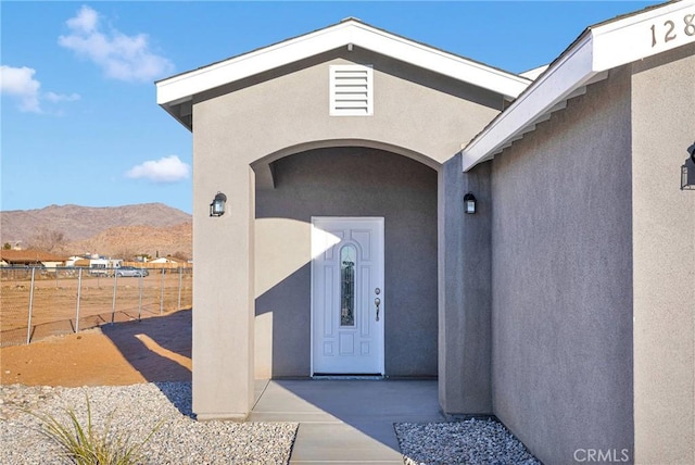 entrance to property featuring a mountain view, fence, and stucco siding