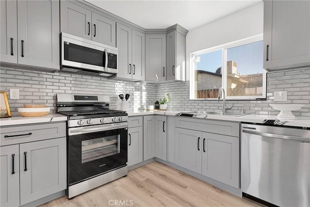 kitchen with stainless steel appliances, a sink, light countertops, gray cabinets, and light wood finished floors