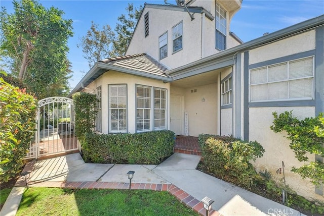 entrance to property with a tile roof, a gate, and stucco siding