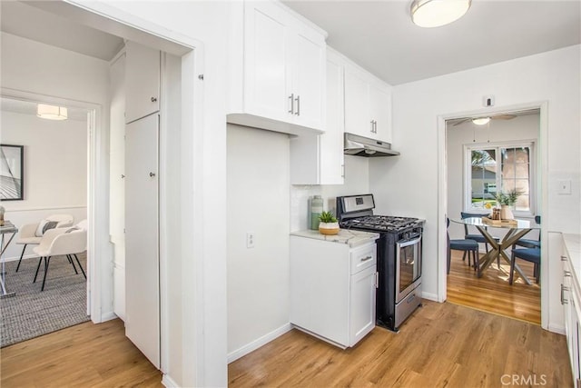 kitchen featuring under cabinet range hood, white cabinetry, light countertops, light wood-type flooring, and stainless steel gas stove