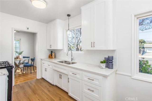 kitchen featuring decorative light fixtures, stove, light wood-style floors, white cabinetry, and a sink