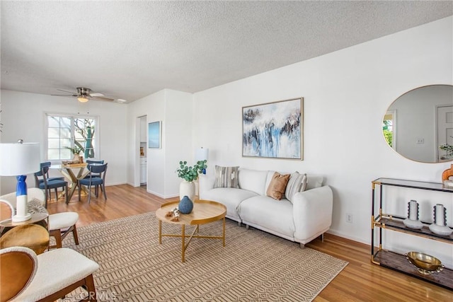 living room with a ceiling fan, light wood-style flooring, baseboards, and a textured ceiling