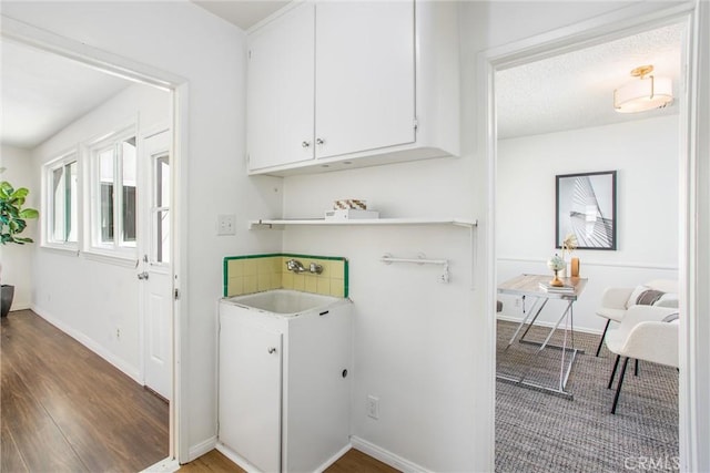 laundry area with wood finished floors, a sink, and baseboards