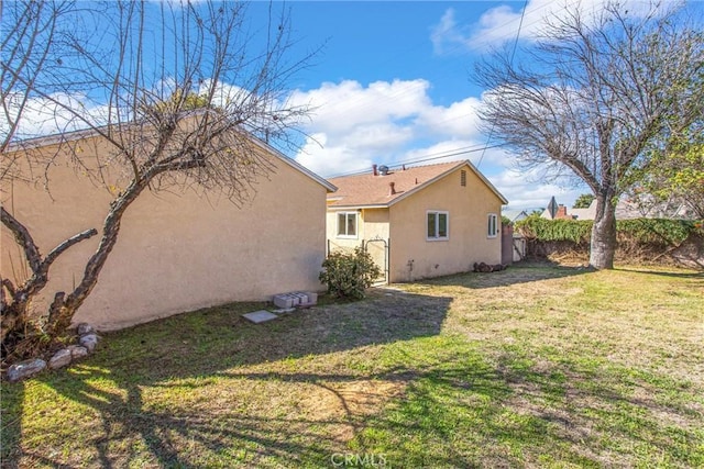 rear view of house with fence, a lawn, and stucco siding