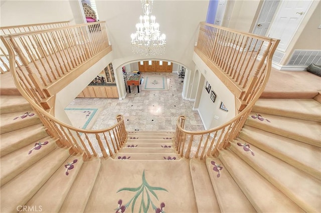 stairway with arched walkways, visible vents, a chandelier, and a towering ceiling