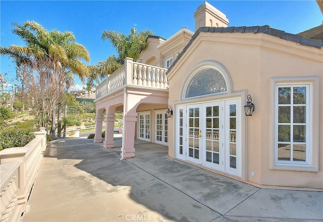 exterior space featuring a balcony, stucco siding, a patio area, and french doors