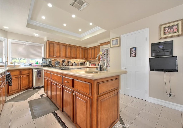 kitchen with stainless steel appliances, a sink, visible vents, a raised ceiling, and a center island with sink