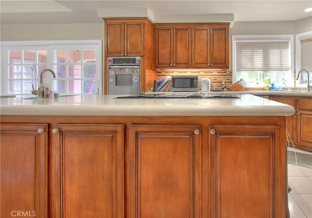 kitchen featuring light tile patterned floors, decorative backsplash, brown cabinets, stainless steel appliances, and a sink