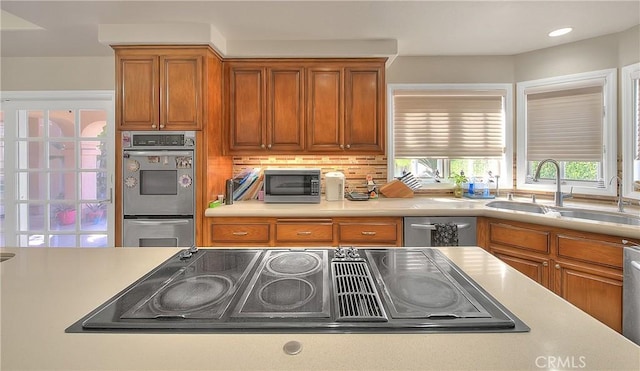 kitchen with brown cabinets, stainless steel appliances, tasteful backsplash, light countertops, and a sink