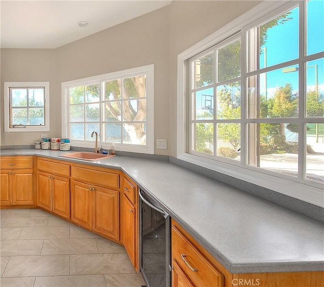 kitchen featuring light tile patterned floors, wine cooler, brown cabinets, light countertops, and a sink