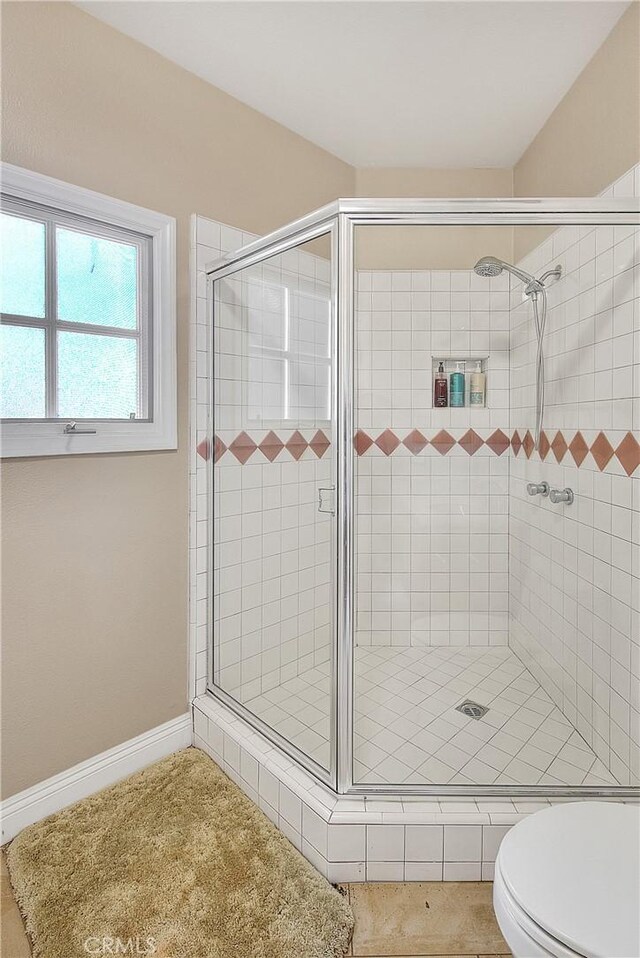 bathroom with a stall shower, toilet, and baseboards