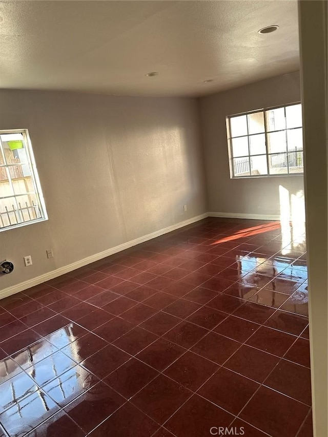 spare room with dark tile patterned flooring, a textured ceiling, and baseboards