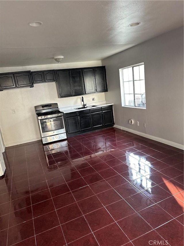 kitchen featuring stainless steel range with gas cooktop, baseboards, light countertops, and a sink