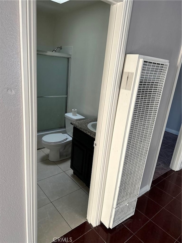 bathroom with a heating unit, toilet, a shower with shower door, tile patterned flooring, and vanity