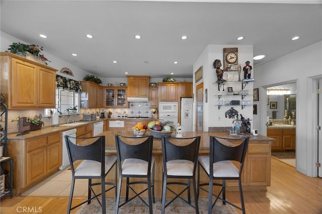 kitchen with white appliances, tasteful backsplash, a kitchen island, glass insert cabinets, and a breakfast bar area